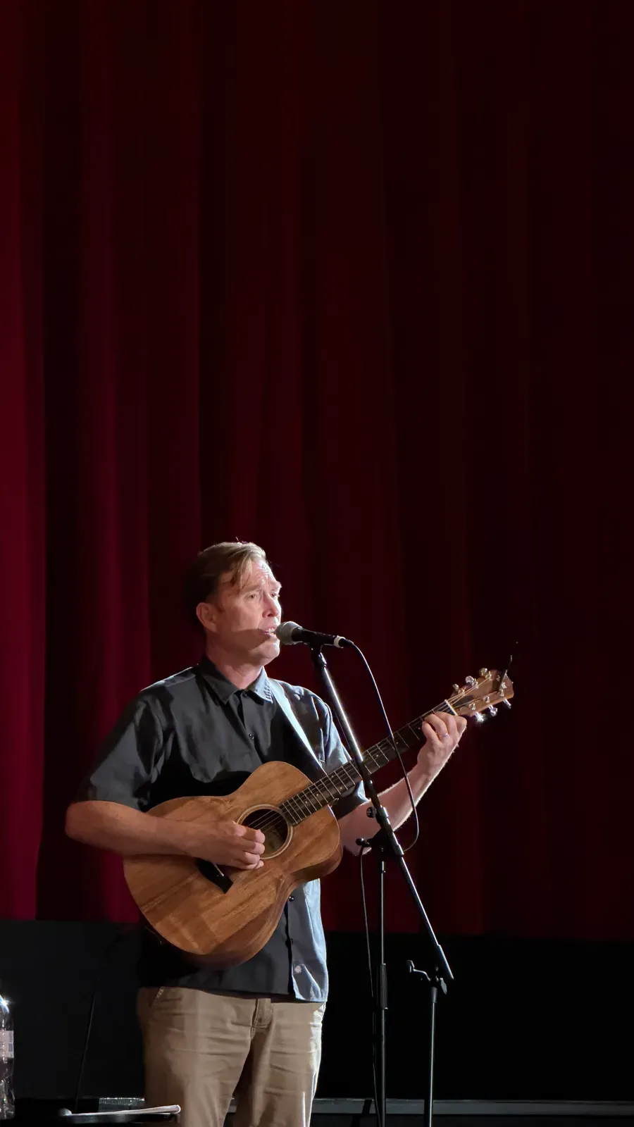 Andy Squyres singt und spielt Akustikgitarre auf der Bühne vor einem roten Vorhang