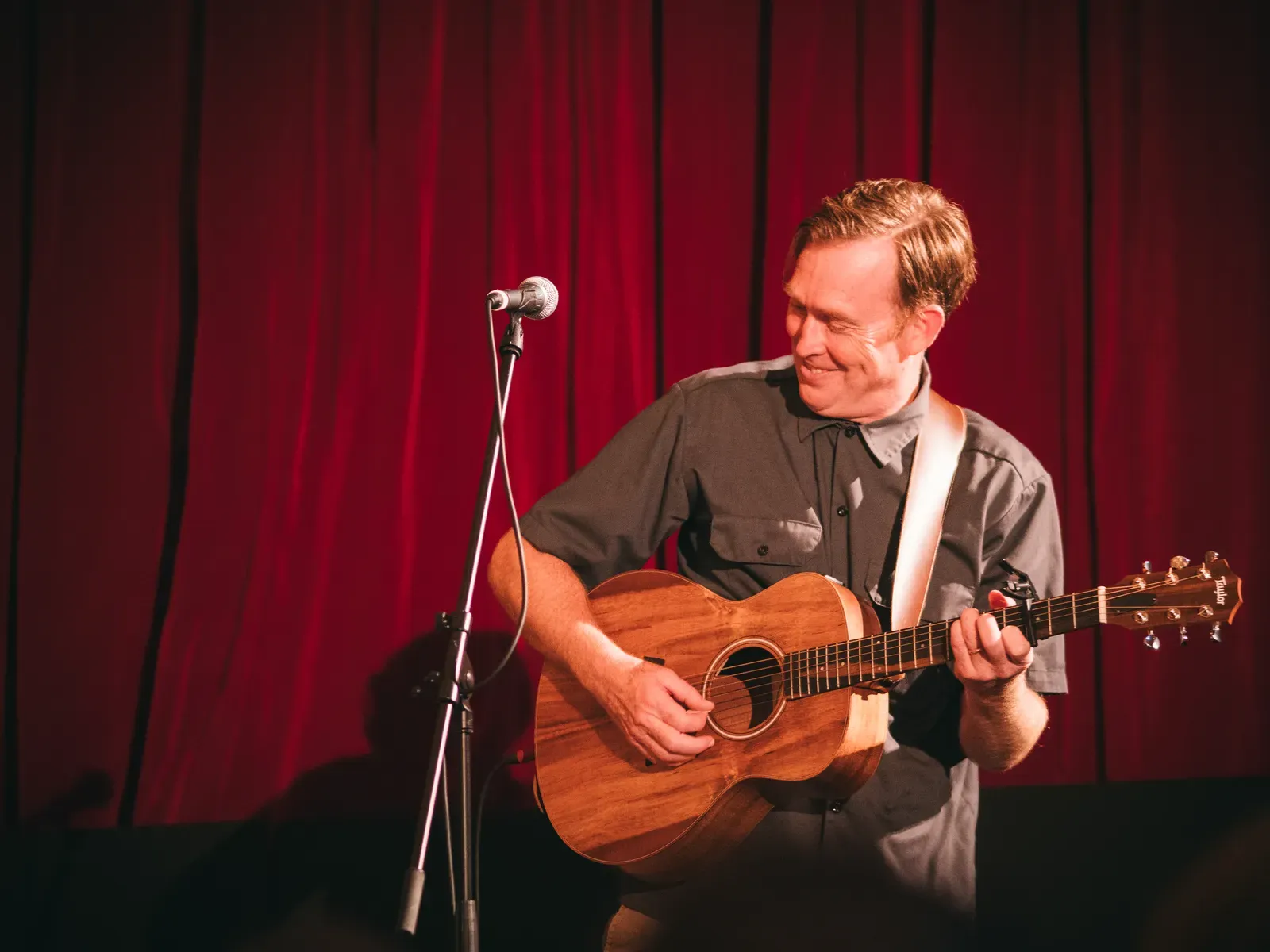 Andy lächelt, während er unter warmem Bühnenlicht Gitarre spielt